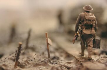 soldier-walking-on-wooden-pathway-surrounded-with-barbwire-selective-focus-photography-qwe8TLRnG8k