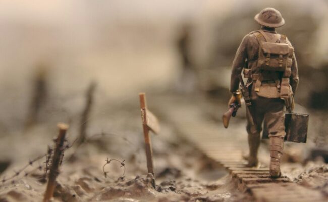 soldier-walking-on-wooden-pathway-surrounded-with-barbwire-selective-focus-photography-qwe8TLRnG8k